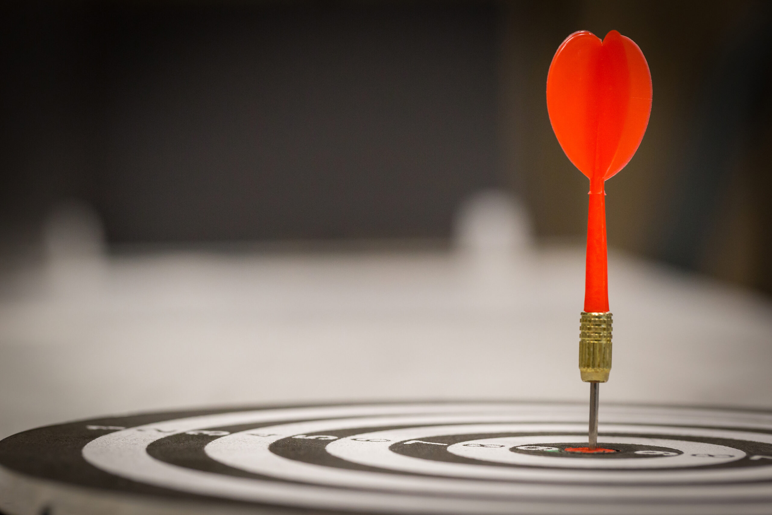 Red dart arrow hitting in the target center of dartboard on bullseye